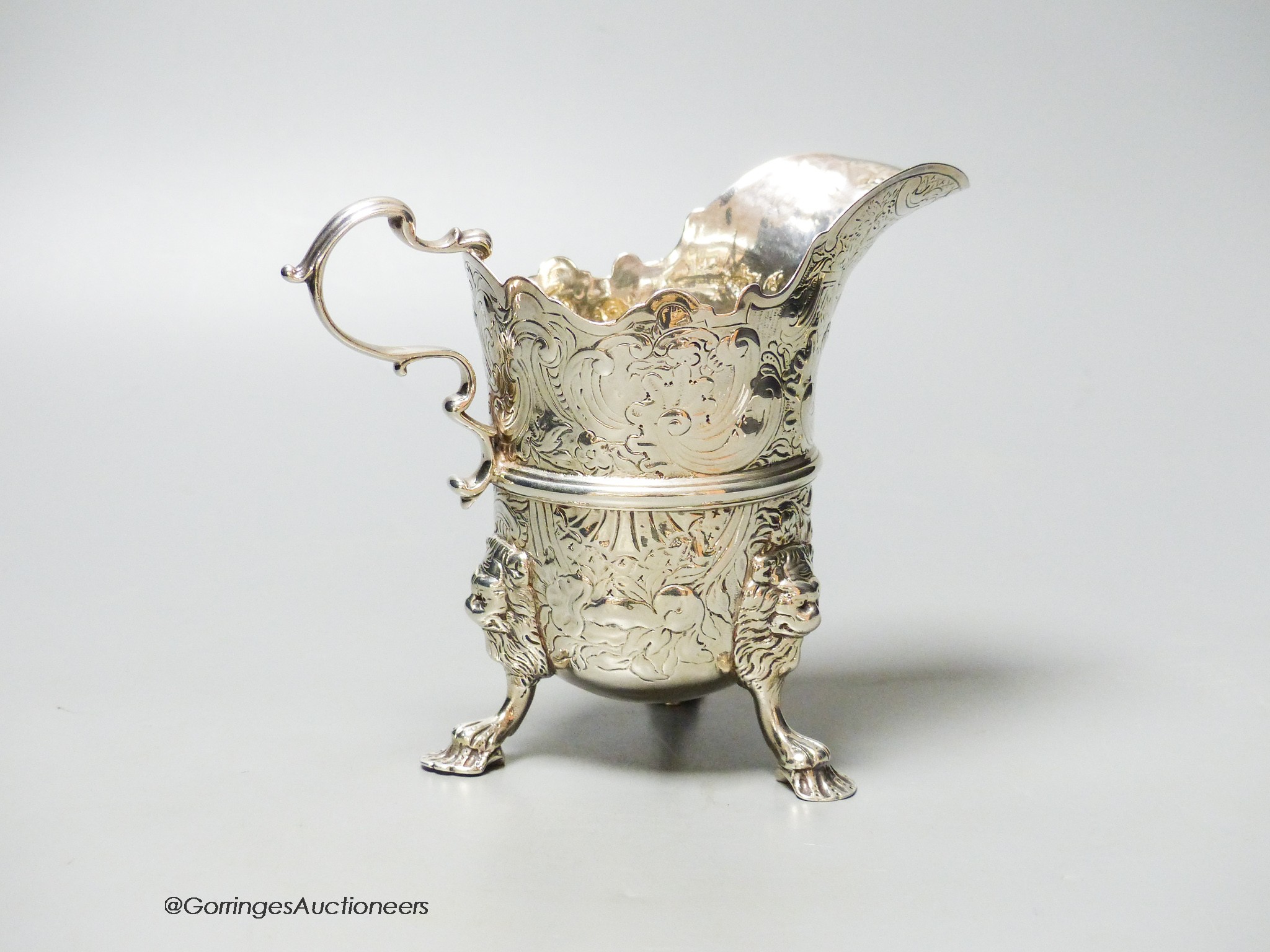 An engraved white metal helmet shaped cream jug, on tripod feet, unmarked, 12.9cm, 9oz.